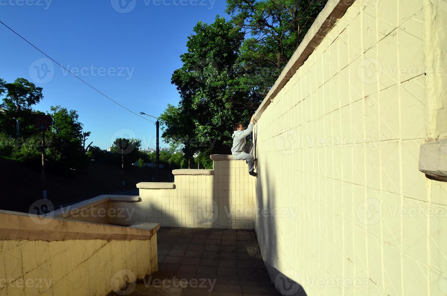 A young guy overcomes obstacles, climbing on concrete walls. The athlete practices parkour, training in street conditions. The concept of sports subcultures among youth photo