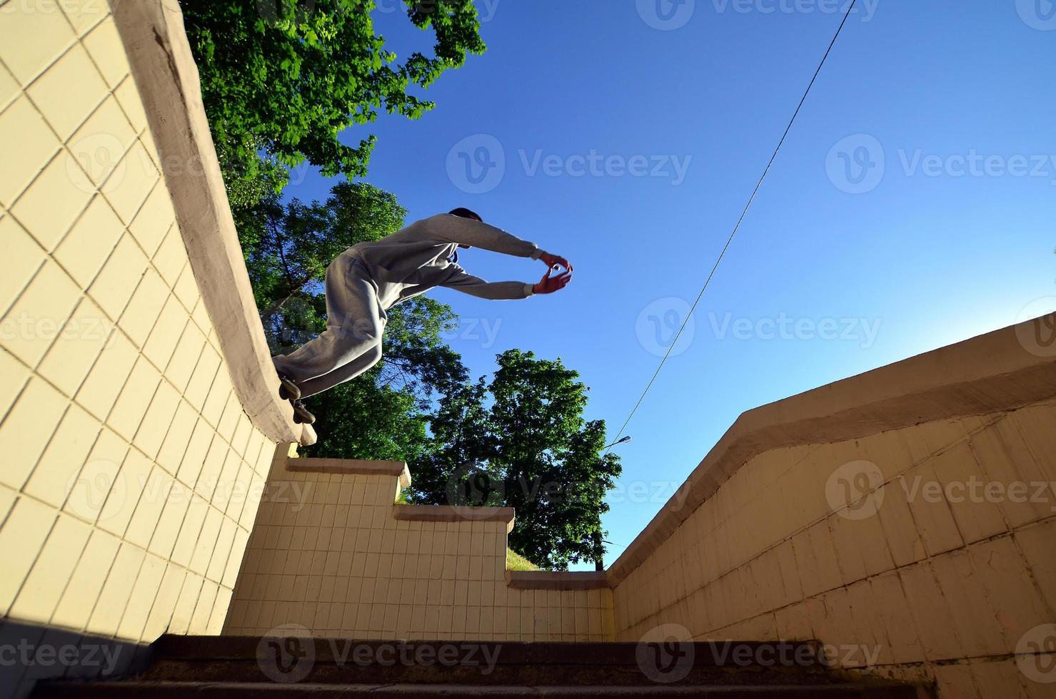 A young guy performs a jump through the space between the concrete parapets. The athlete practices parkour, training in street conditions. Bottom view photo