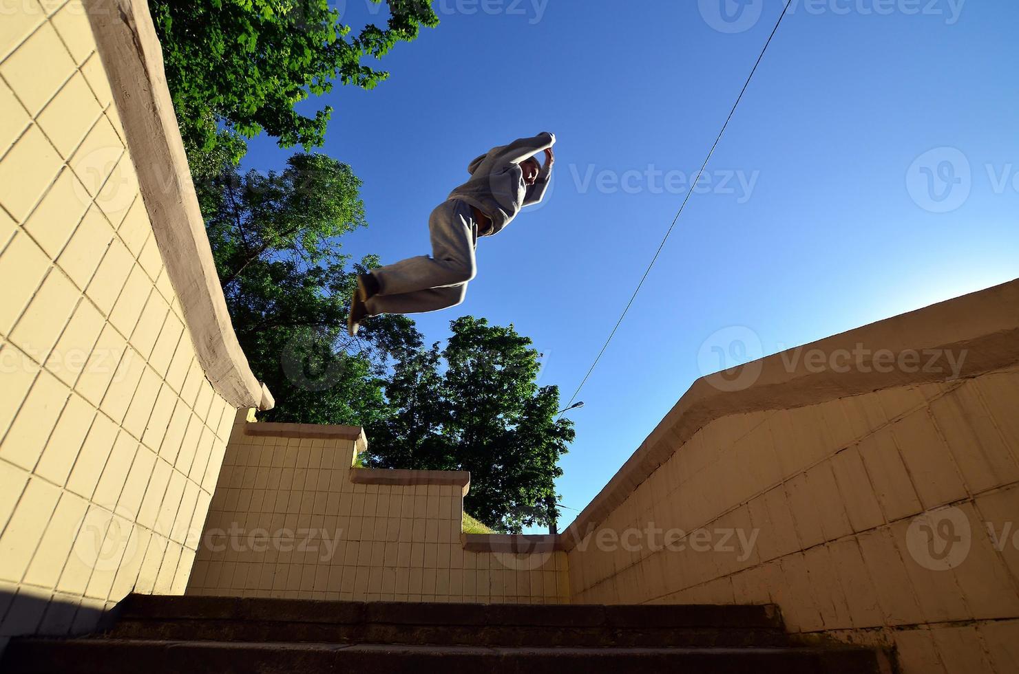 A young guy performs a jump through the space between the concrete parapets. The athlete practices parkour, training in street conditions. Bottom view photo