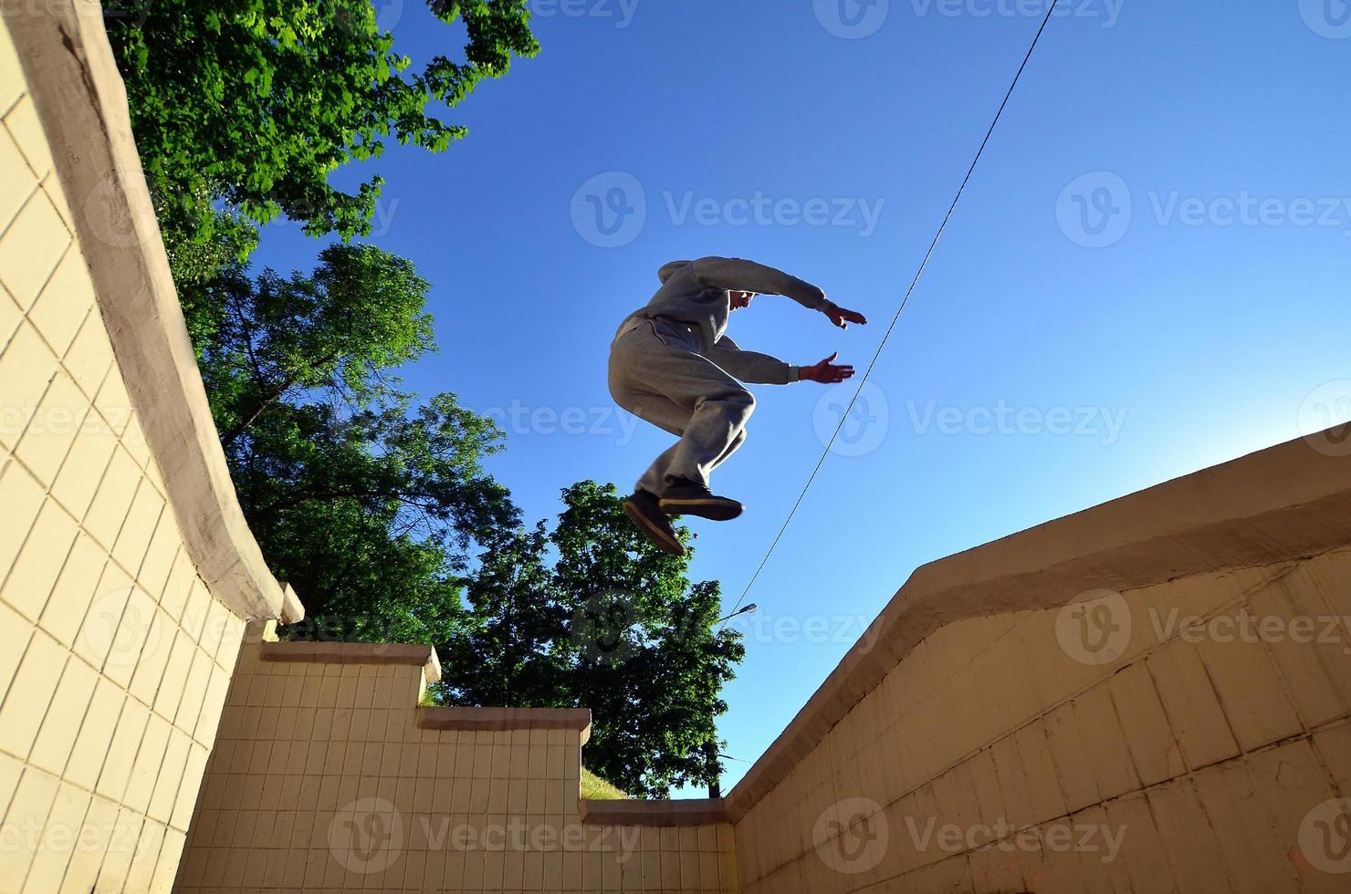 A young guy performs a jump through the space between the concrete parapets. The athlete practices parkour, training in street conditions. Bottom view photo