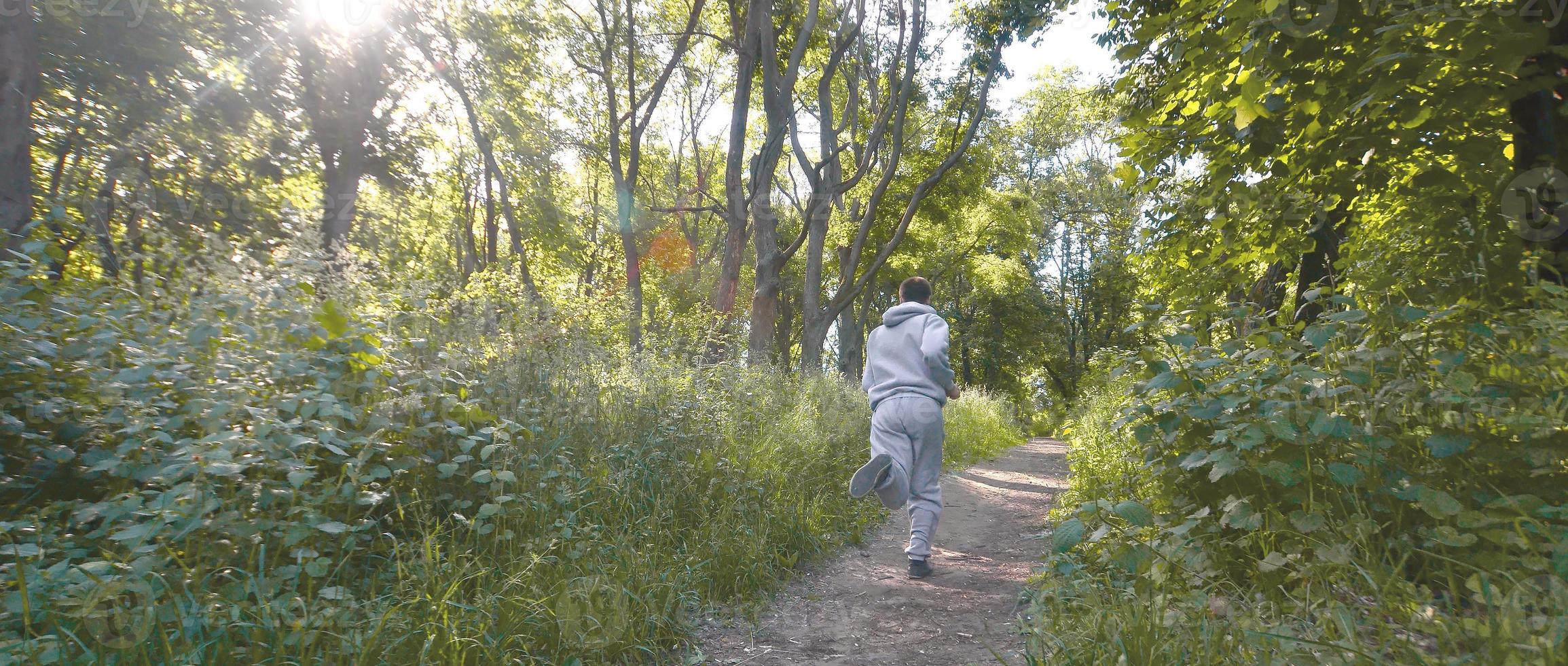un joven con un traje deportivo gris corre por el camino entre los foto