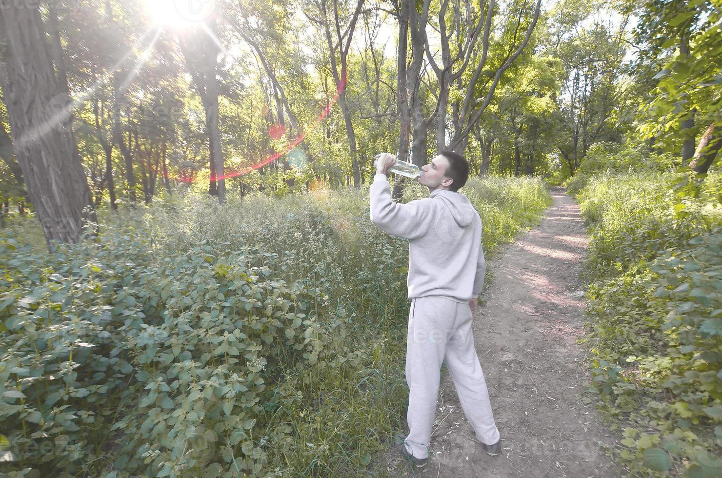 A young guy in a gray sports suit drinks water from a bottle amo photo