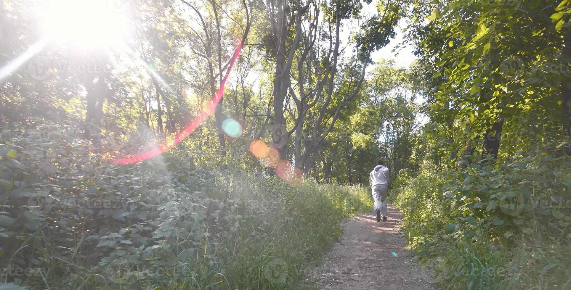 A young guy in a gray sports suit runs along the path among the photo