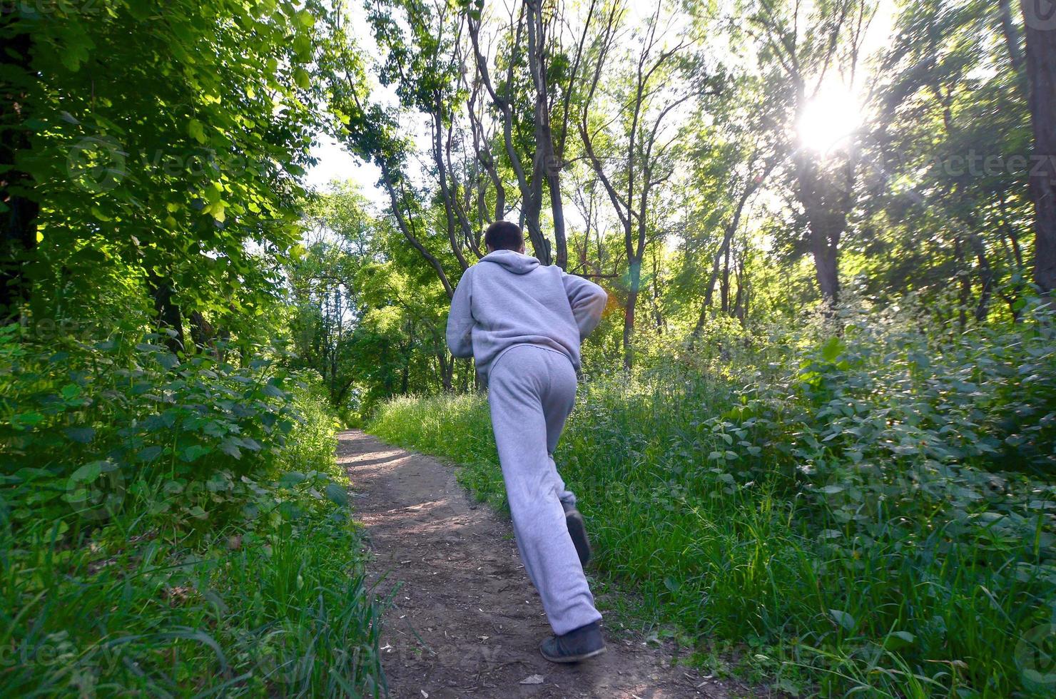 A young guy in a gray sports suit runs along the path among the photo