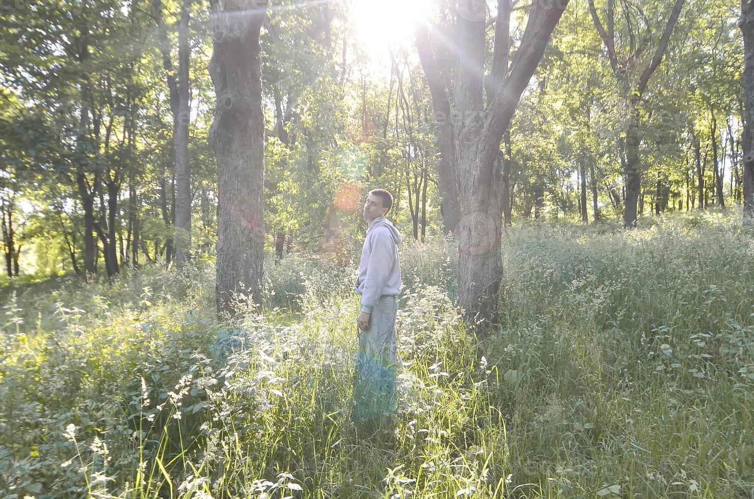 A young guy in a gray sports suit stands opposite the sun among photo