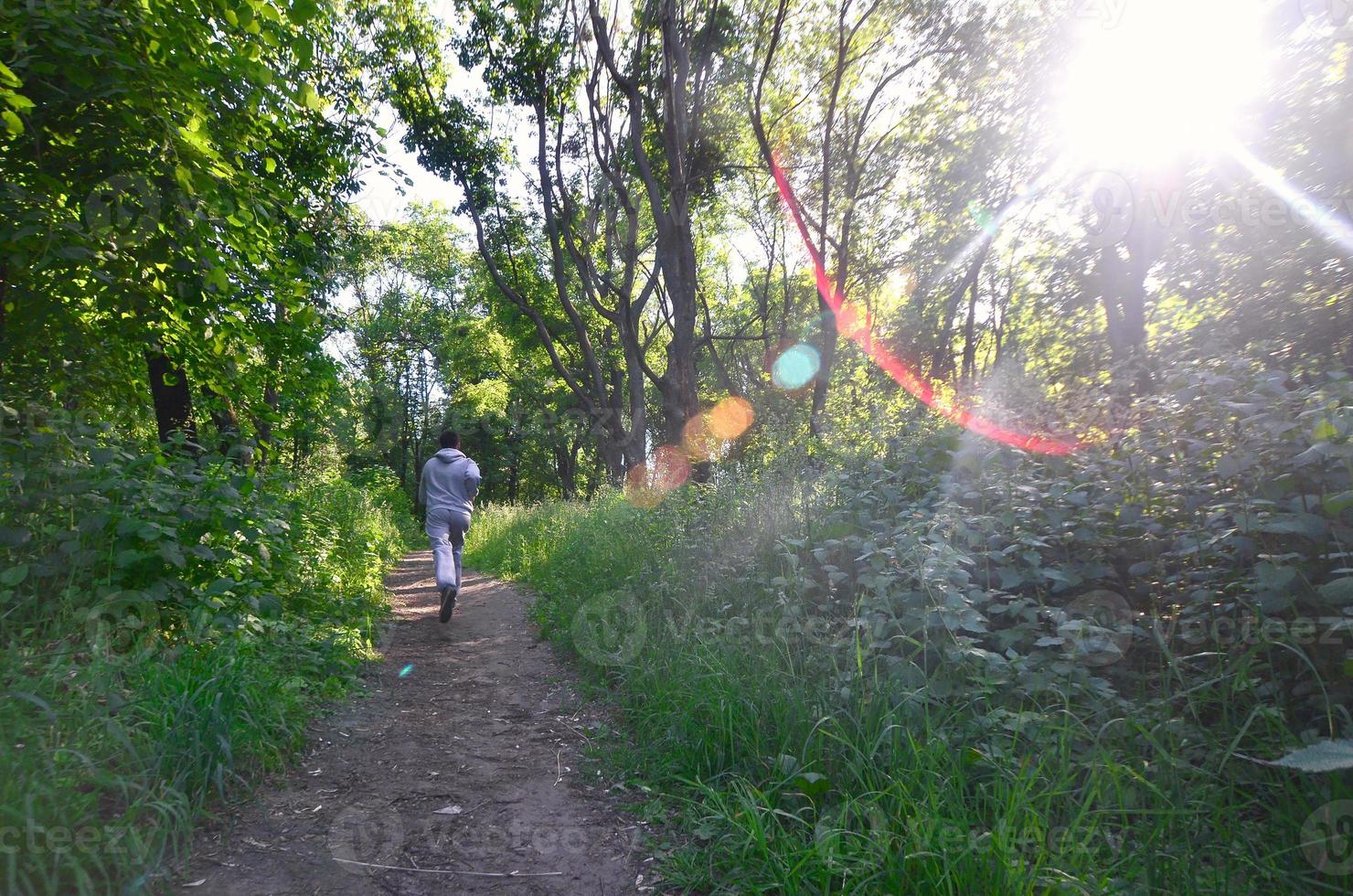 A young guy in a gray sports suit runs along the path among the photo