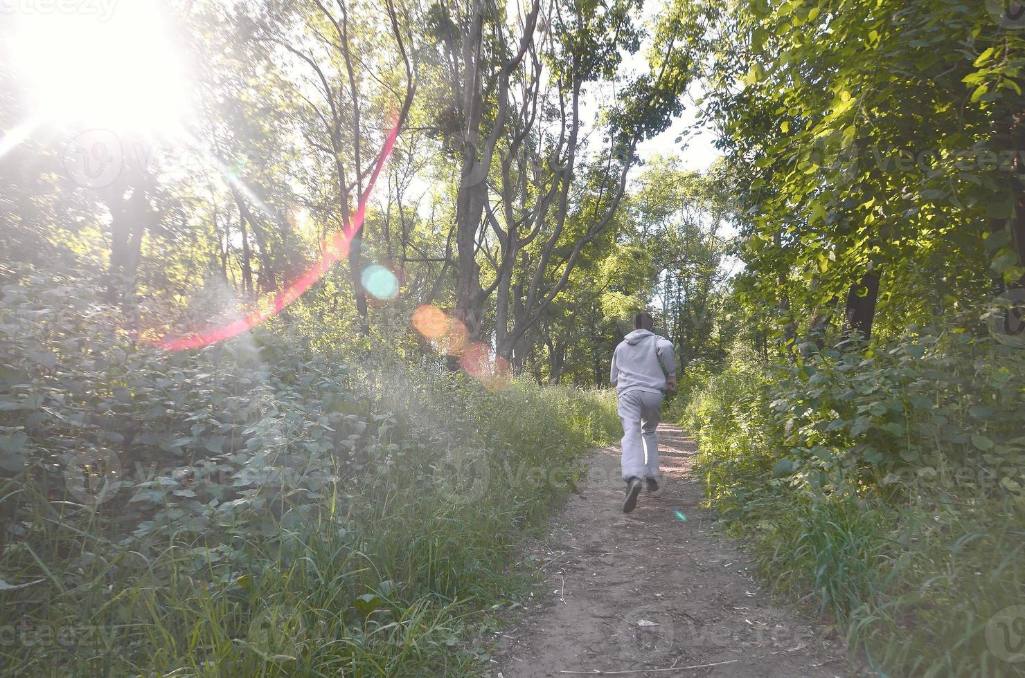 A young guy in a gray sports suit runs along the path among the photo