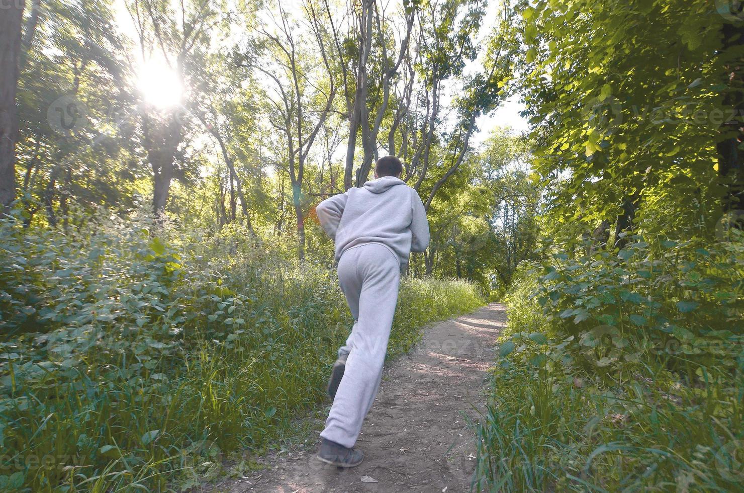 A young guy in a gray sports suit runs along the path among the photo