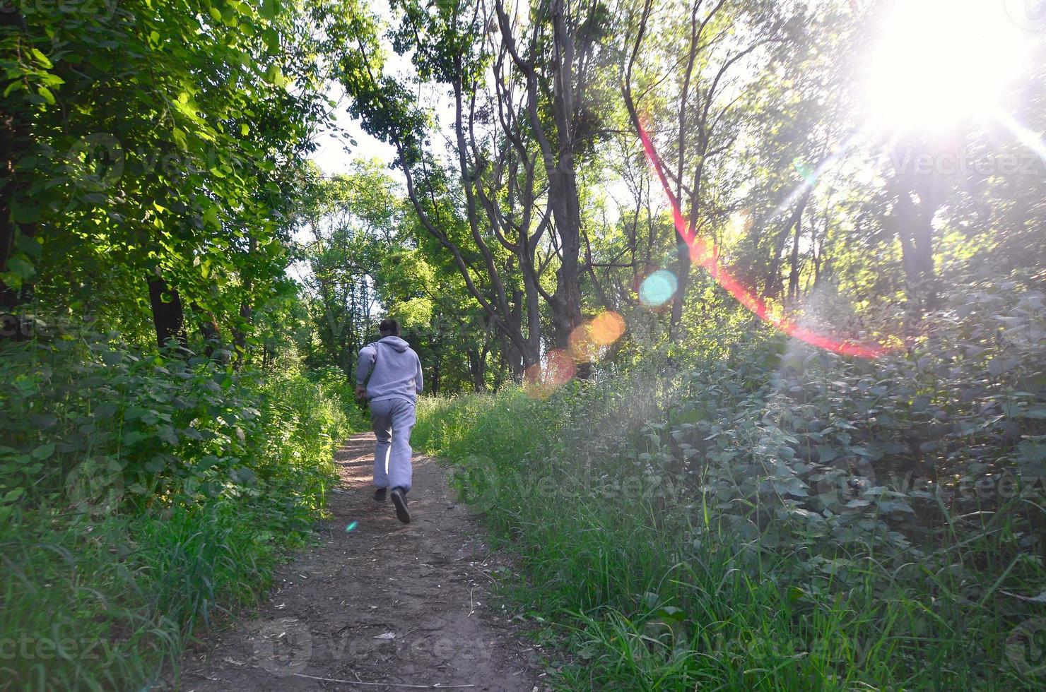 A young guy in a gray sports suit runs along the path among the photo