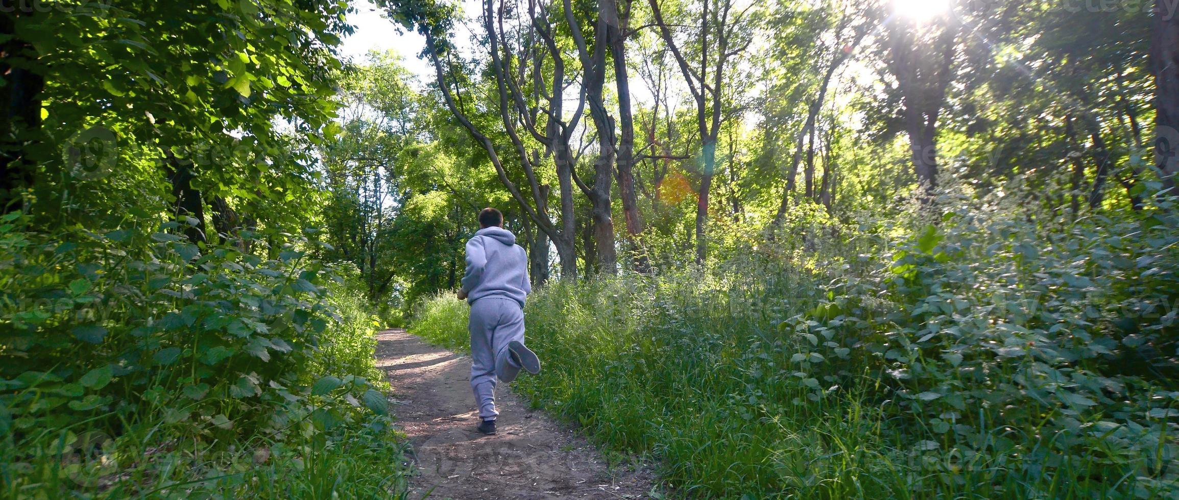 A young guy in a gray sports suit runs along the path among the photo