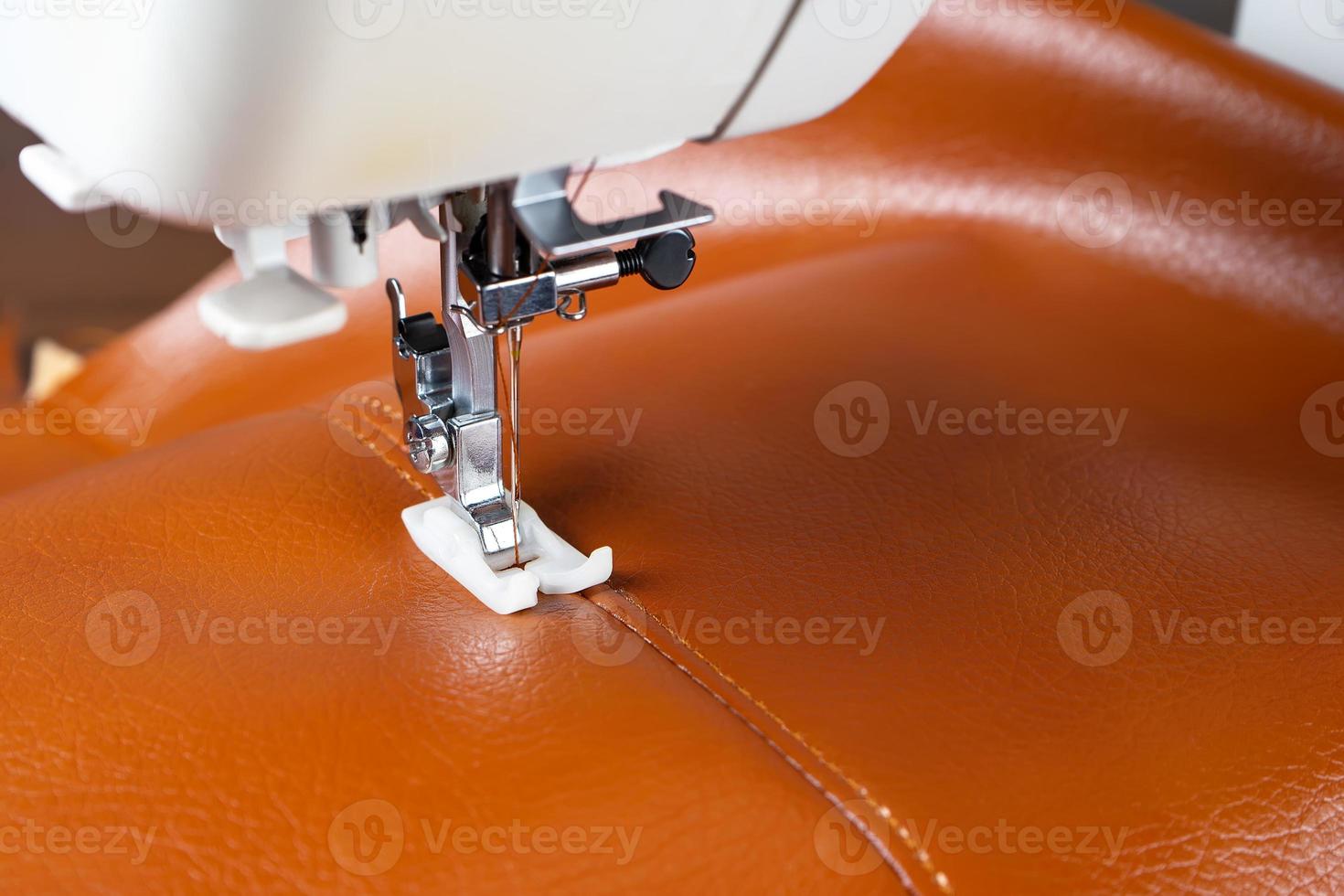 Modern sewing machine presser foot with a needle sews brown leather photo