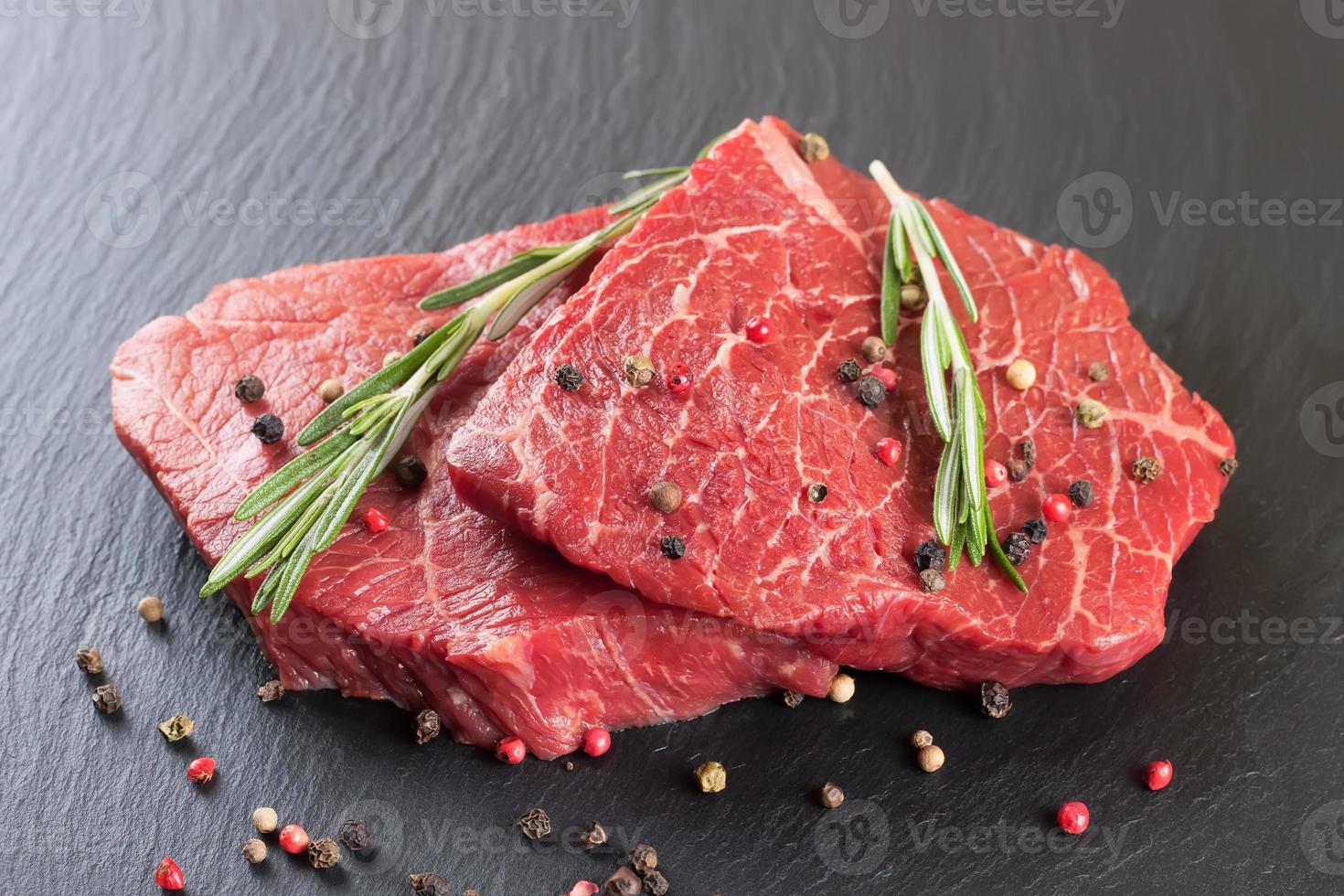 bistec de ternera cruda fresca con especias sobre fondo de pizarra negra foto