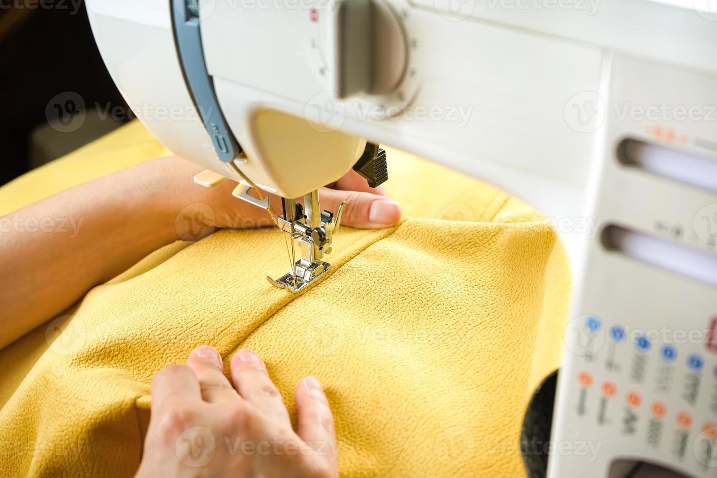 manos femeninas cosiendo tela amarilla en una máquina de coser moderna. vista de cerca del proceso de costura. foto