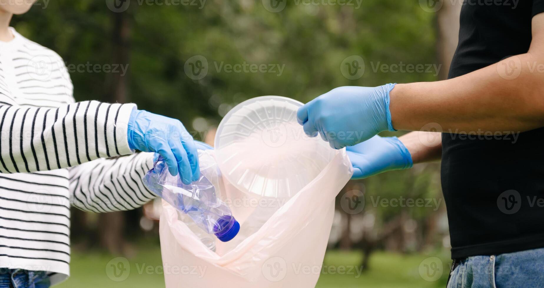 Two people keeping garbage plastic bottle into black bag at park.Clearing, pollution, ecology and plastic concept. photo