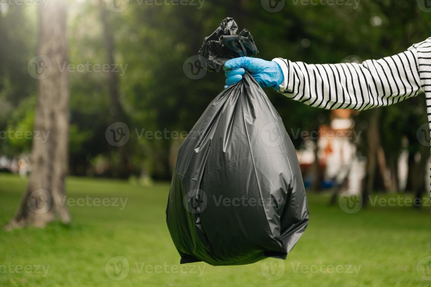 Hand holding garbage black bag putting in to trash to clean. Clearing, pollution, and plastic concept. photo