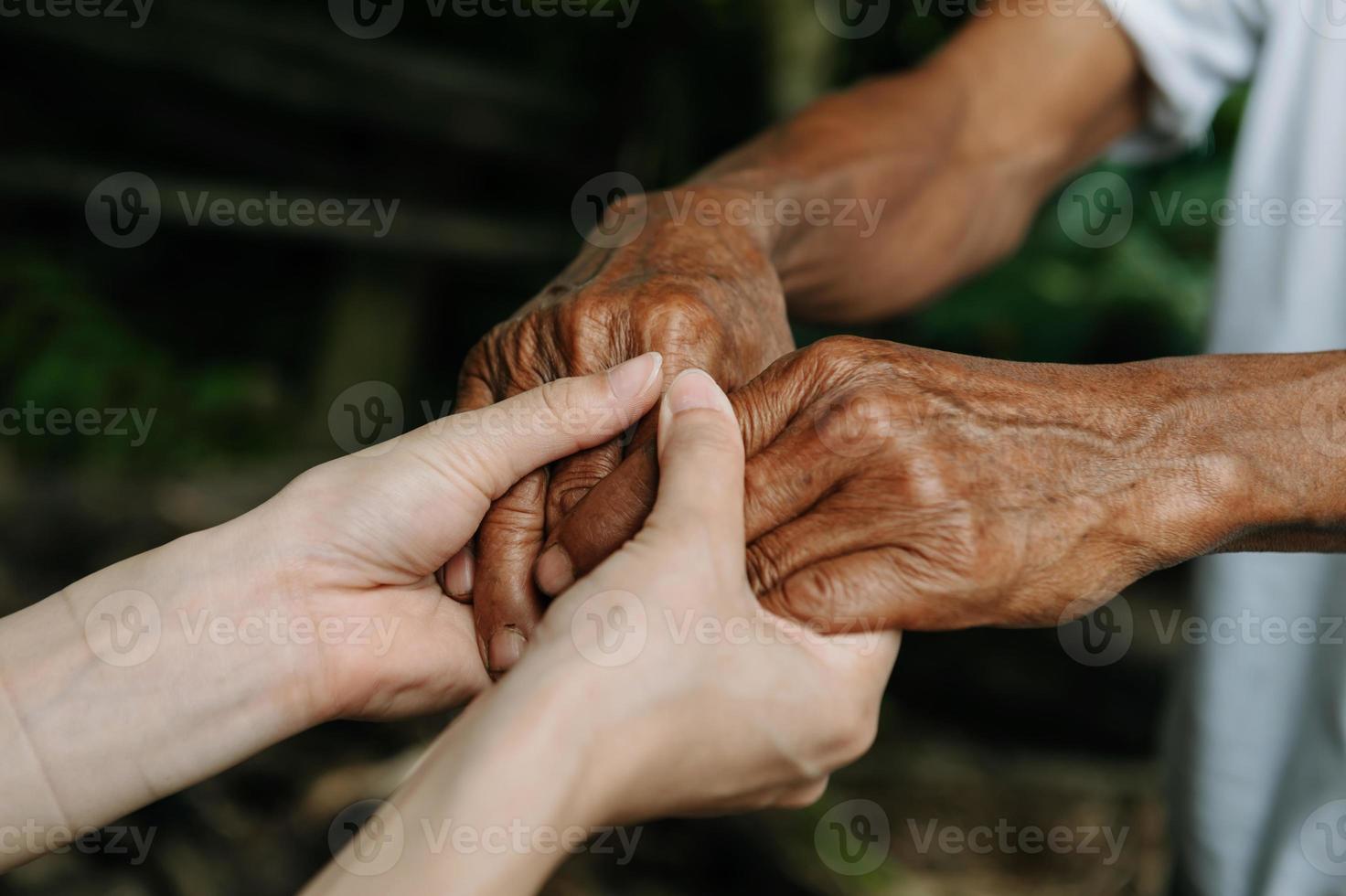 manos del anciano y una mano de mujer en la mesa de madera a la luz del sol foto