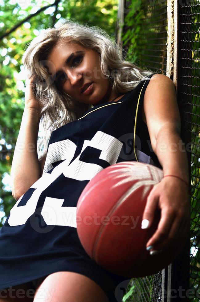 Young blonde girl with orange basketball posing outdoors photo