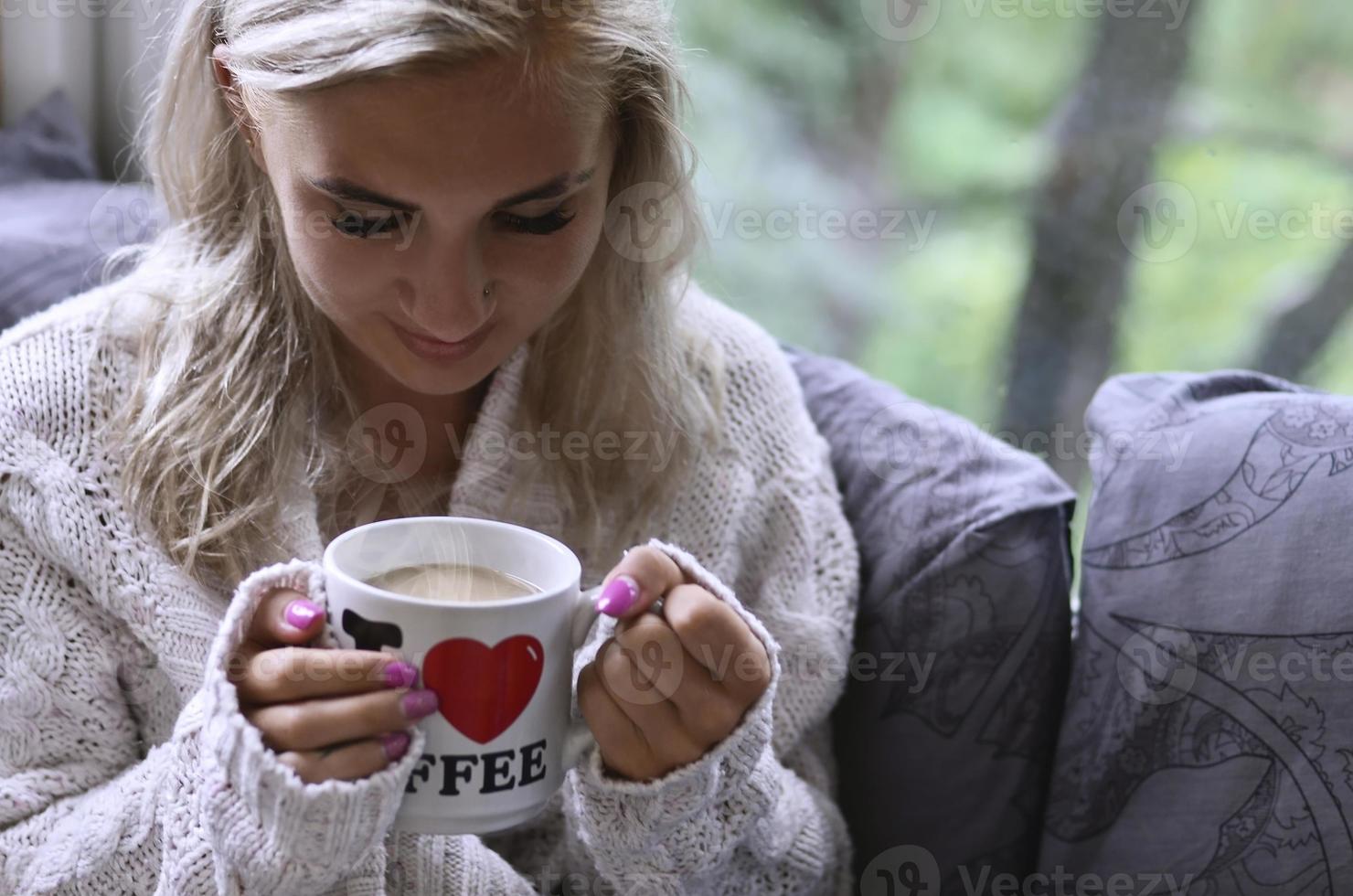 Blonde girl in a warm sweater with a cup of coffee sitting on a photo
