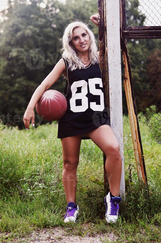 jovencita rubia con baloncesto naranja posando al aire libre foto