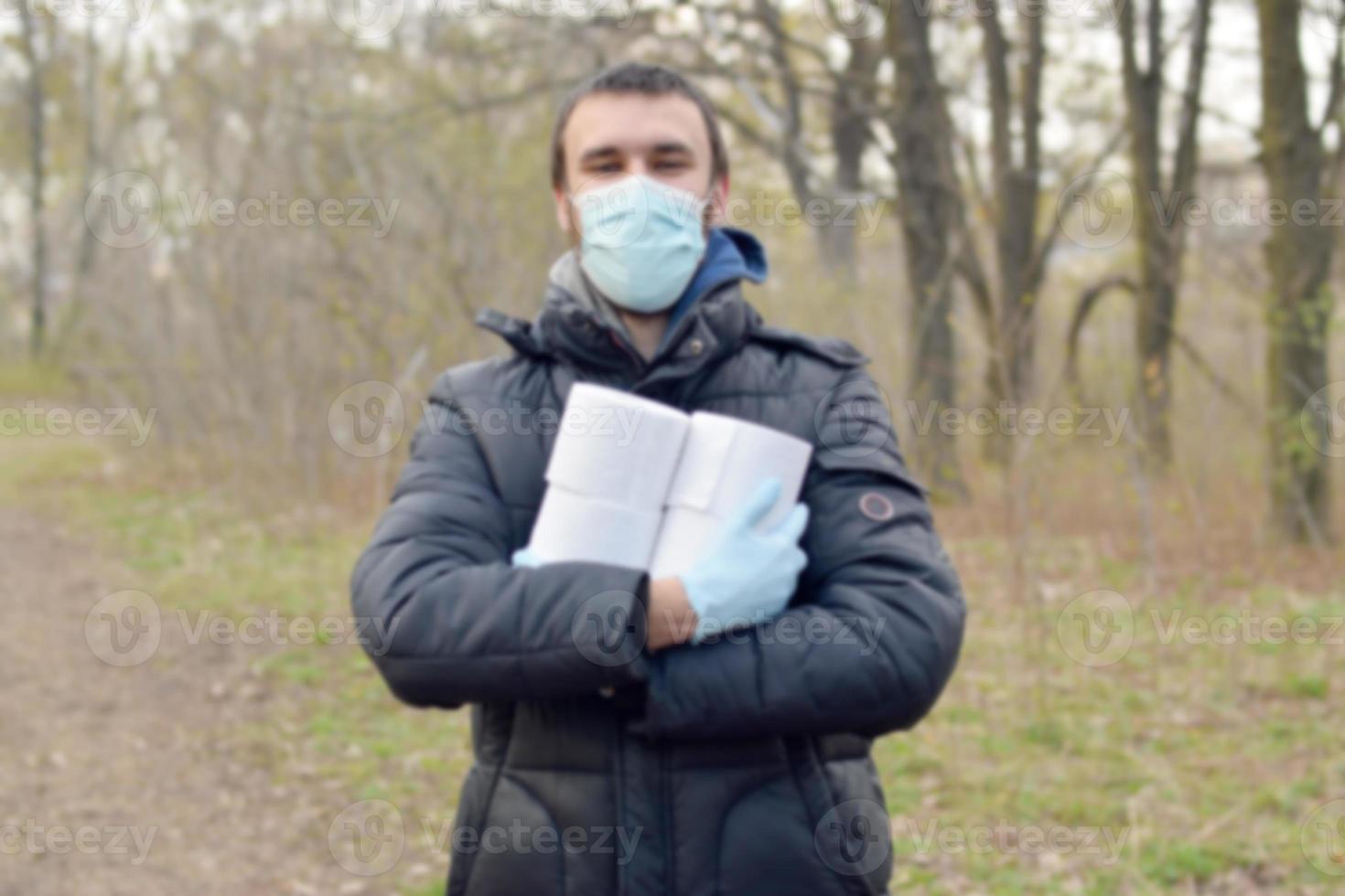 Covidiot concept. Blurred young man in protective mask holds many rolls of toilet paper outdoors in spring wood photo