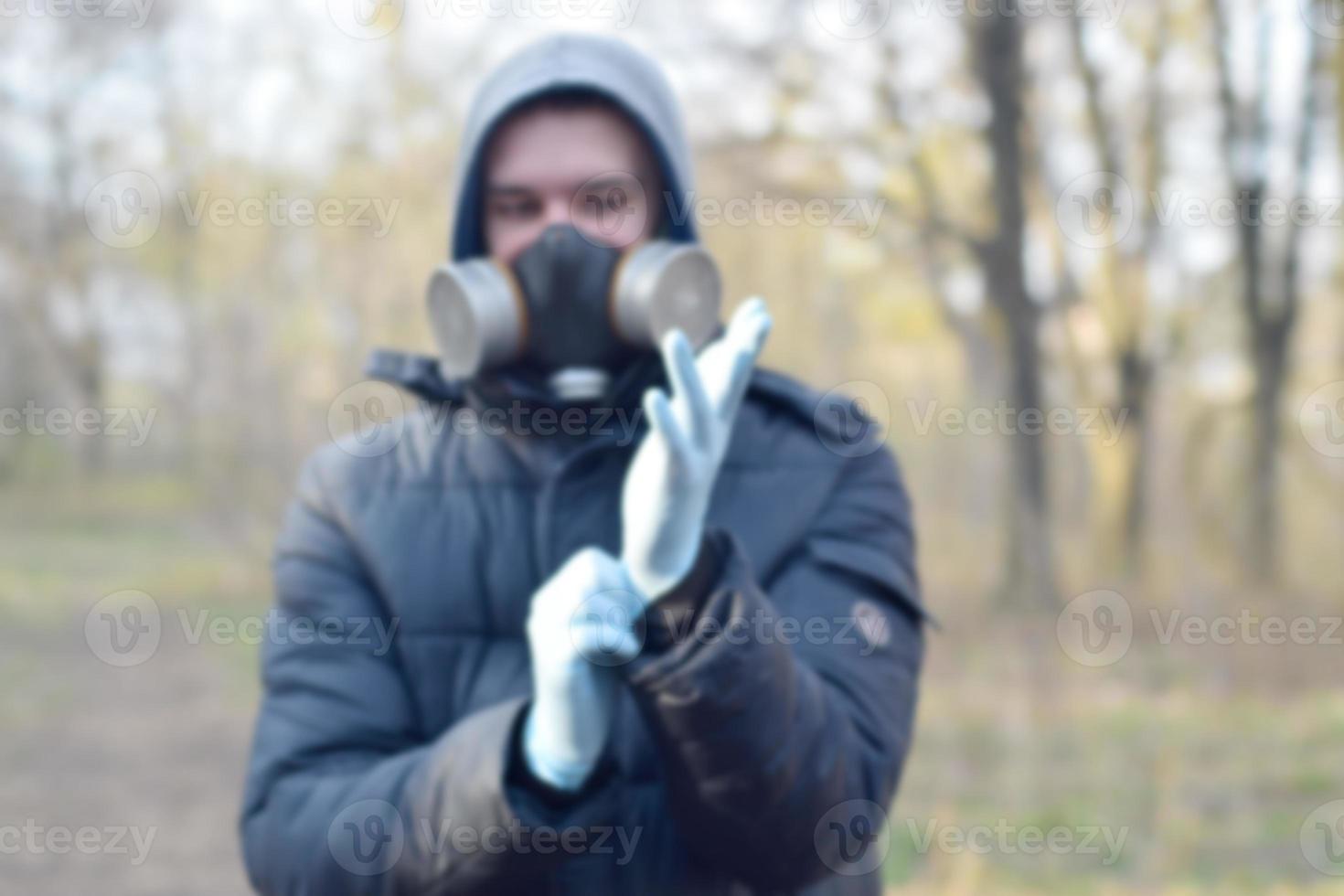 Blurred portrait of young man in protective gas mask wears rubber disposable gloves outdoors in spring wood photo
