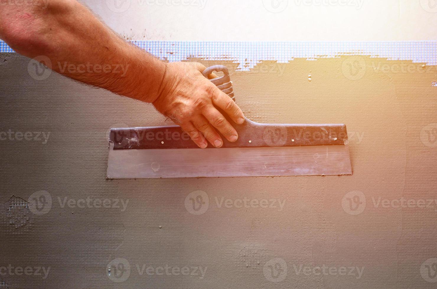 Hands of an old manual worker with wall plastering tools renovating house. Plasterer renovating outdoor walls and corners with spatula and plaster. Wall insulation. Construction finishing works photo