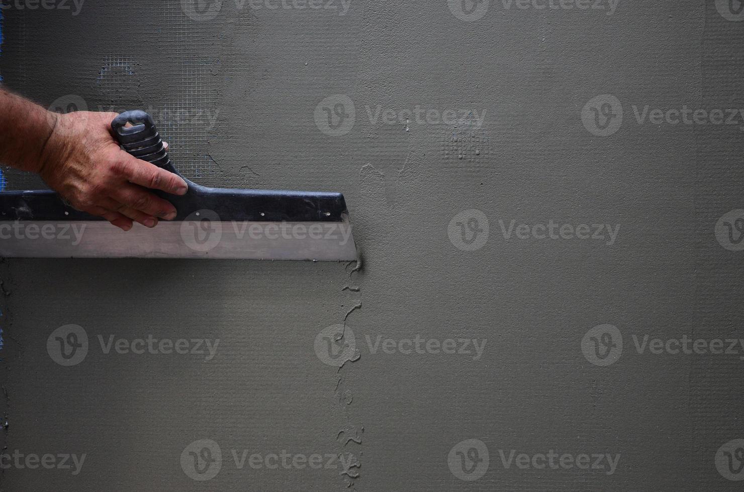 Hands of an old manual worker with wall plastering tools renovating house. Plasterer renovating outdoor walls and corners with spatula and plaster. Wall insulation. Construction finishing works photo