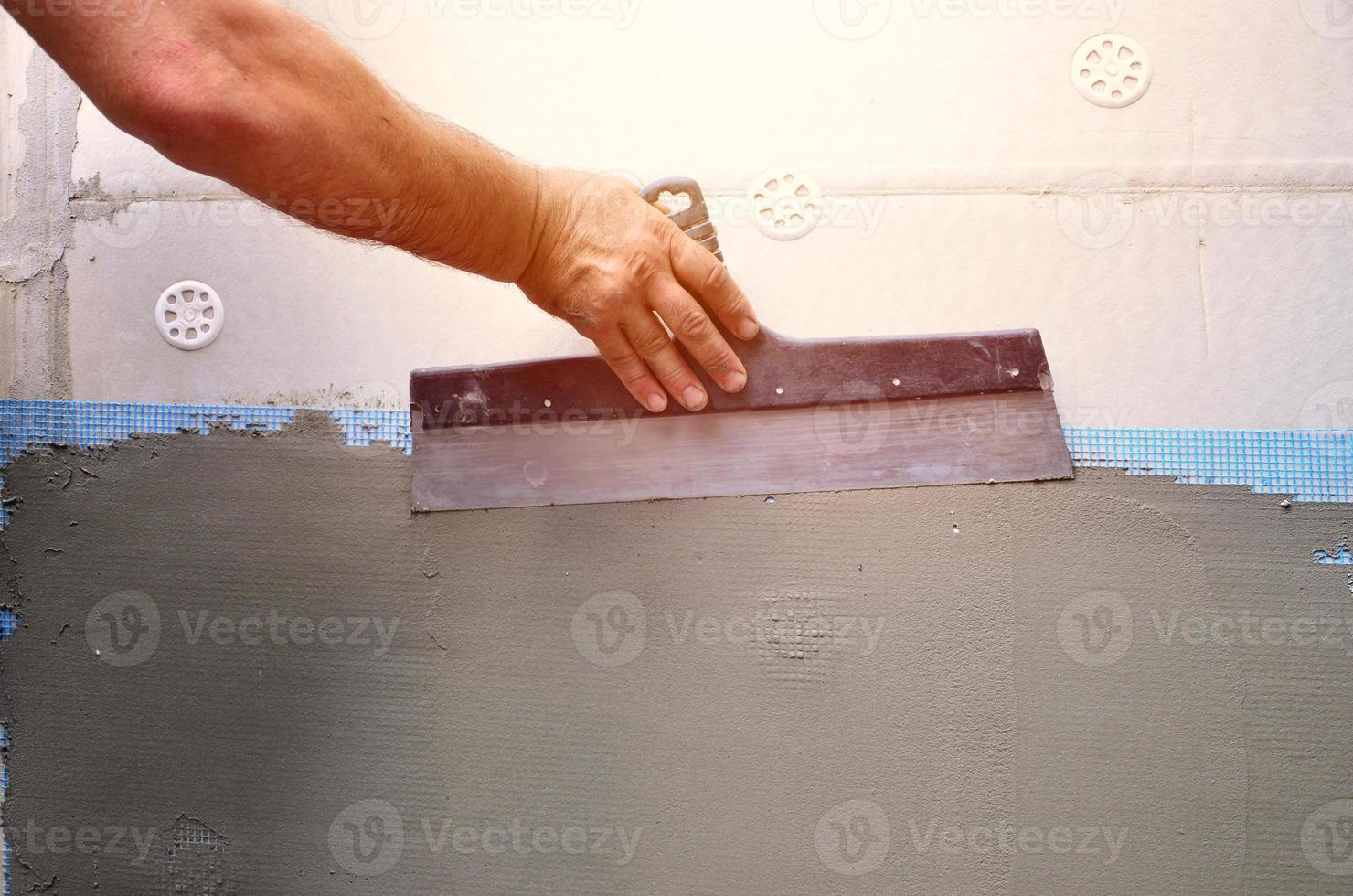 Hands of an old manual worker with wall plastering tools renovating house. Plasterer renovating outdoor walls and corners with spatula and plaster. Wall insulation. Construction finishing works photo