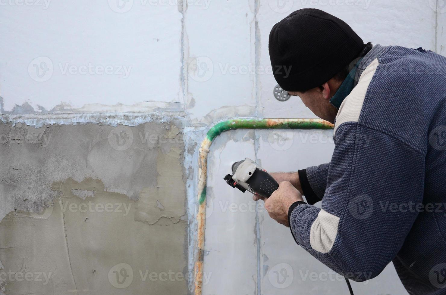 An elderly workman drills a hole in a styrofoam wall for the subsequent installation of a plastic reinforcing dowel. Creating holes in the wall with a drill. Warming of the building facade photo