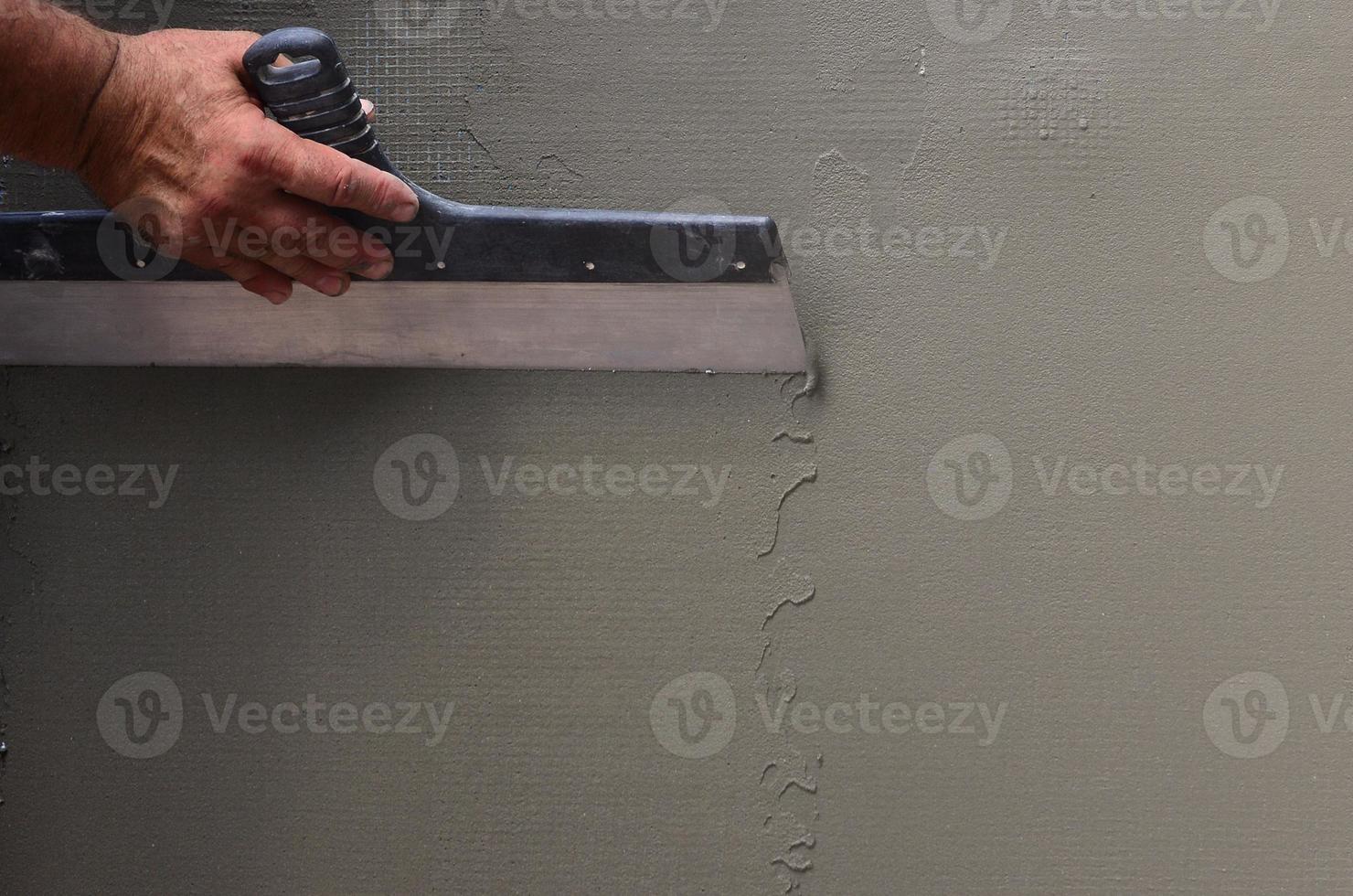 Hands of an old manual worker with wall plastering tools renovating house. Plasterer renovating outdoor walls and corners with spatula and plaster. Wall insulation. Construction finishing works photo