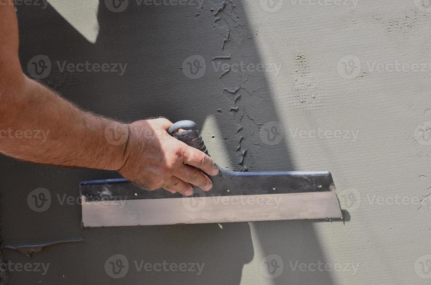 Hands of an old manual worker with wall plastering tools renovating house. Plasterer renovating outdoor walls and corners with spatula and plaster. Wall insulation. Construction finishing works photo