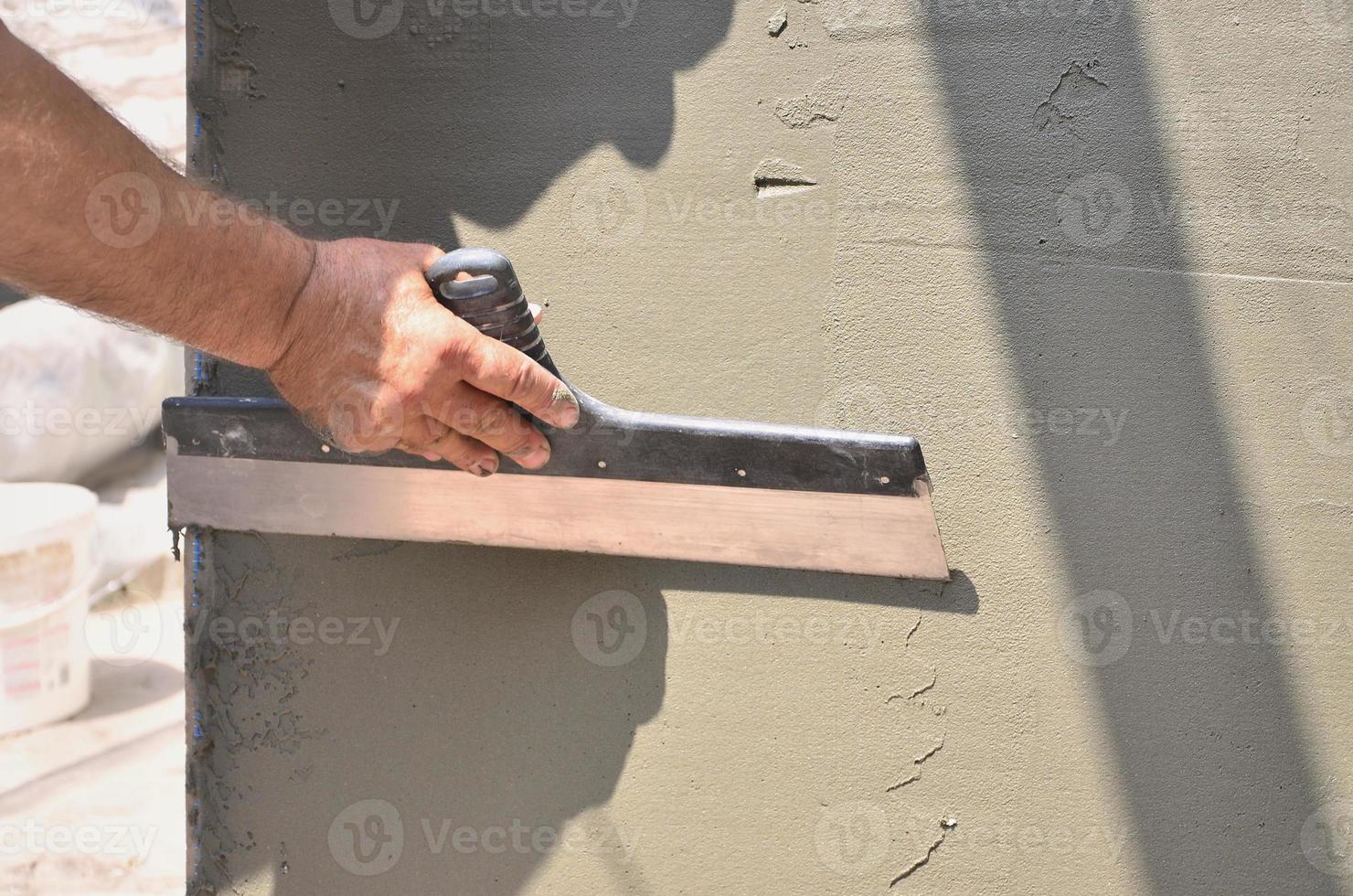 Hands of an old manual worker with wall plastering tools renovating house. Plasterer renovating outdoor walls and corners with spatula and plaster. Wall insulation. Construction finishing works photo