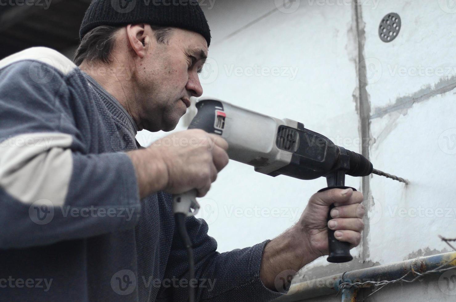 An elderly workman drills a hole in a styrofoam wall for the subsequent installation of a plastic reinforcing dowel. Creating holes in the wall with a drill. Warming of the building facade photo