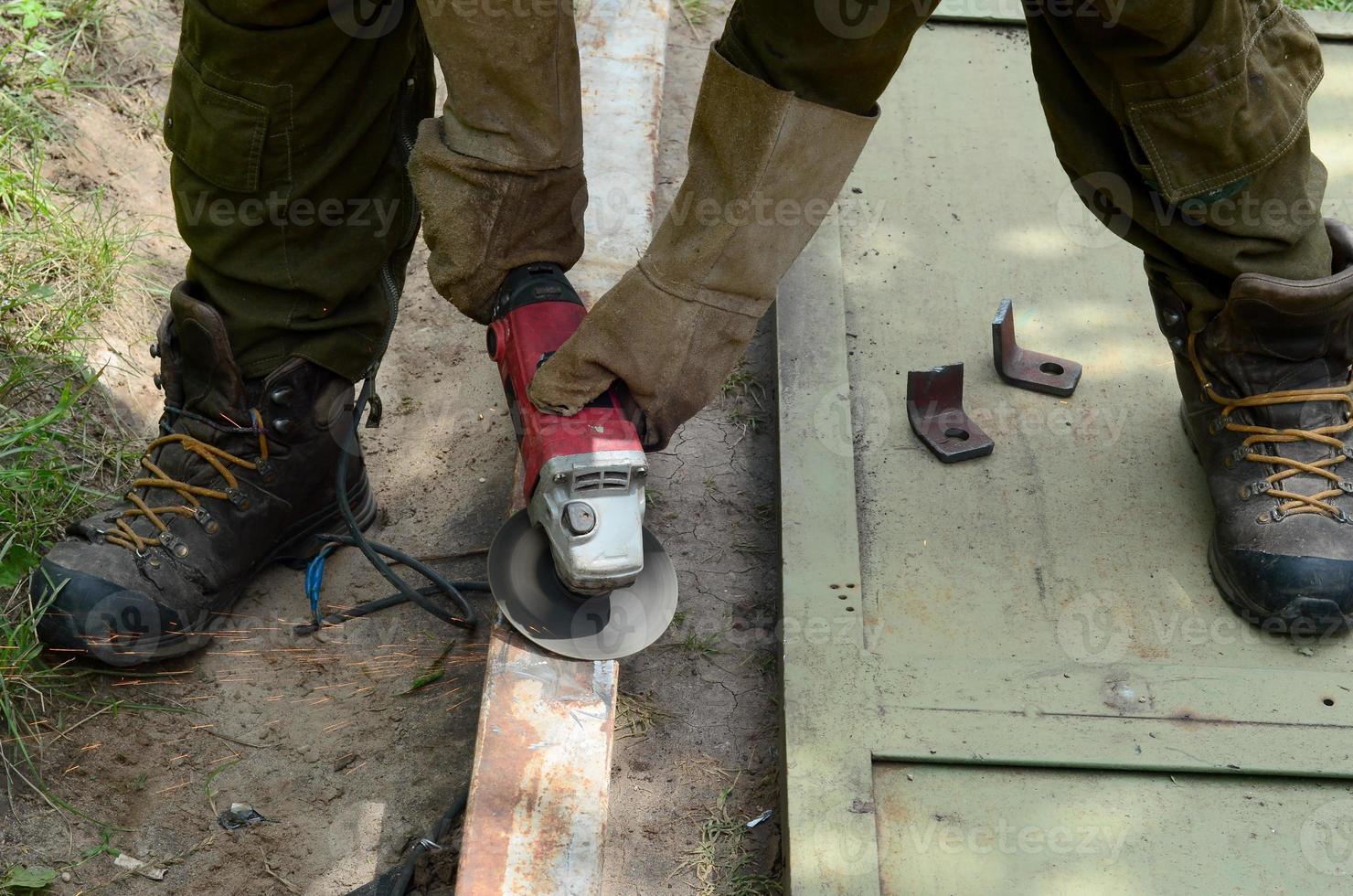 Electric wheel grinding on steel structure outdoors. Old manual worker in protective gloves cutting metal door with grinder photo