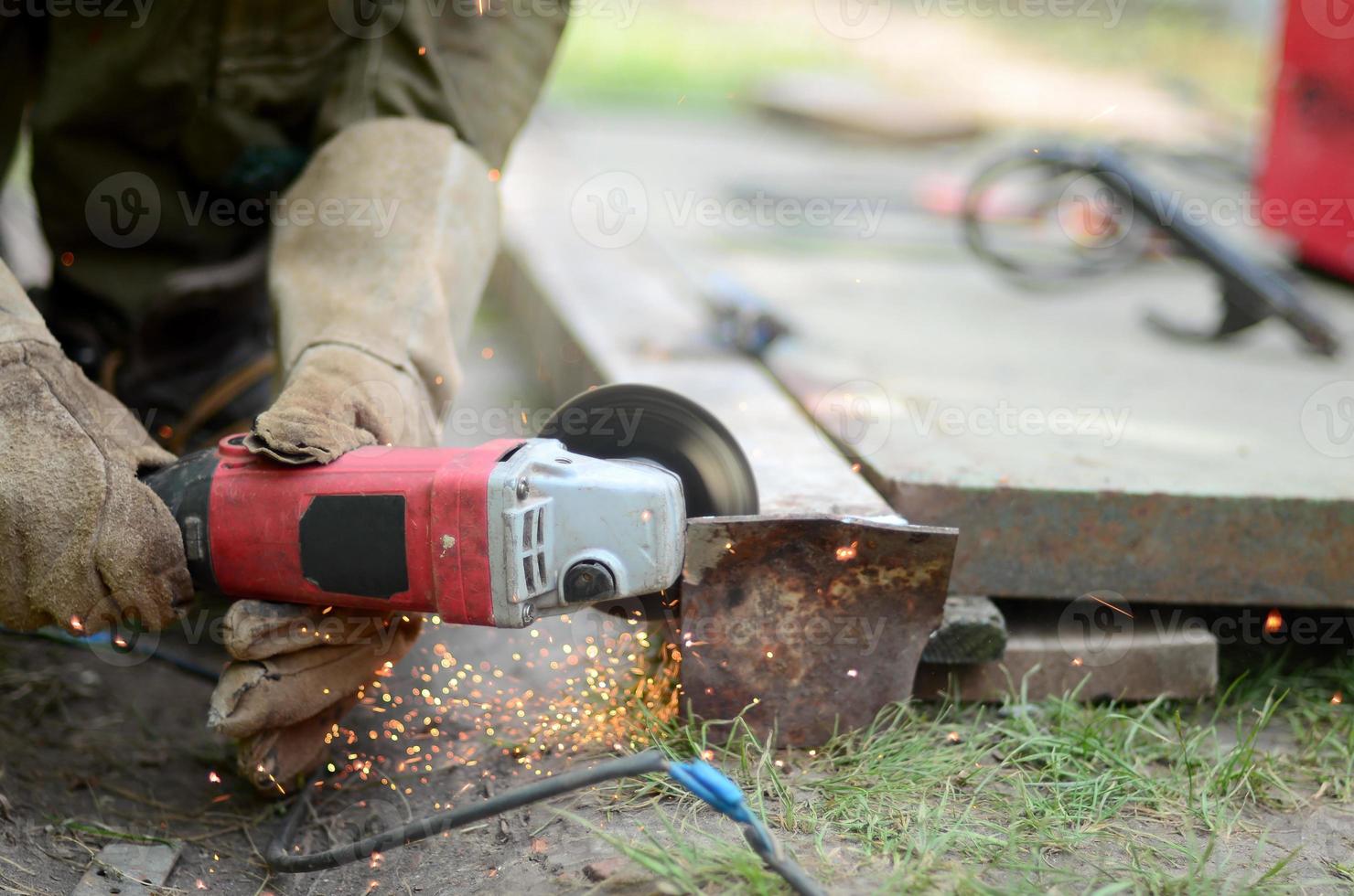 Rectificado eléctrico de ruedas en estructura de acero al aire libre. viejo trabajador manual con guantes protectores cortando puertas de metal con molinillo foto