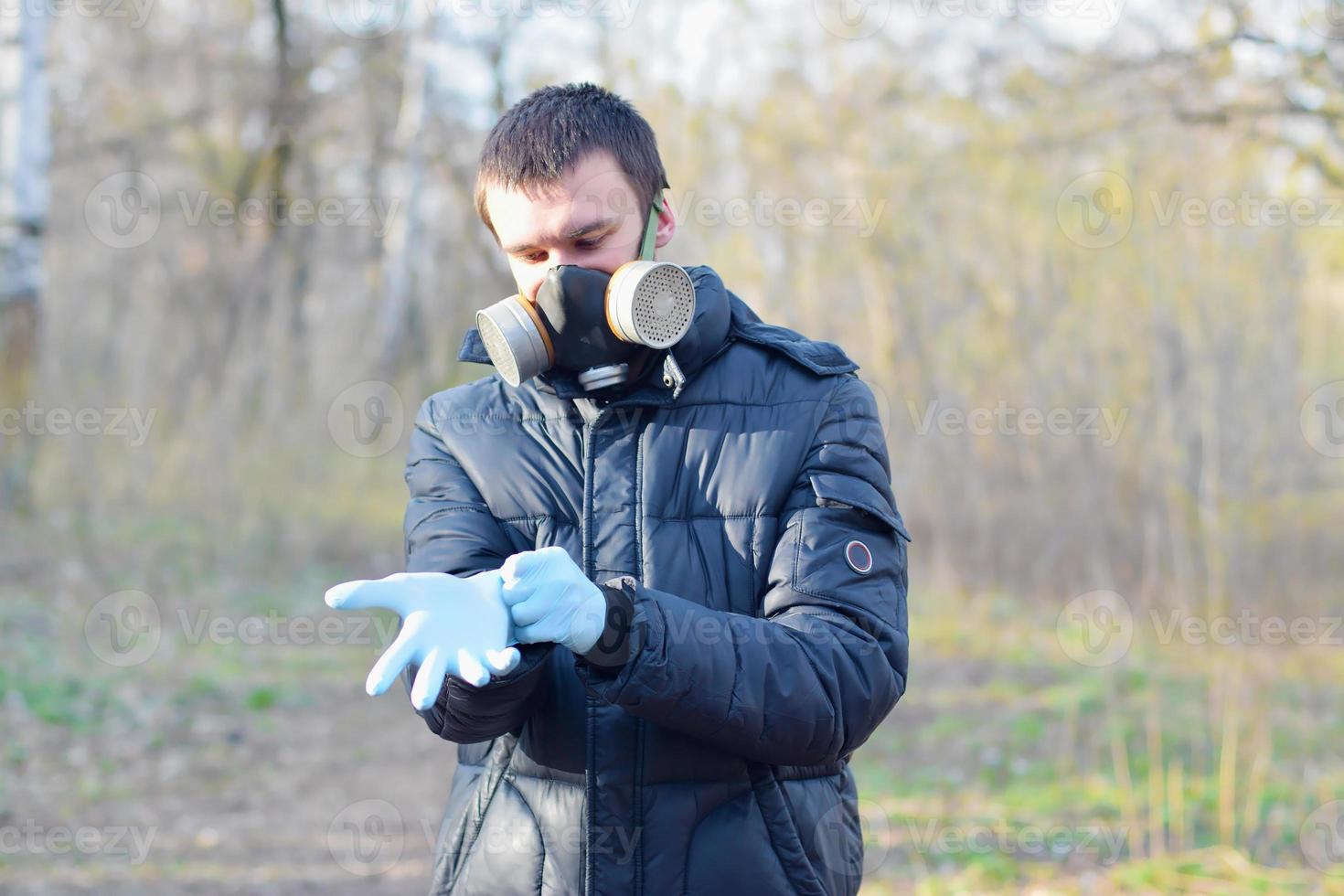 Portrait of young man in protective gas mask wears rubber disposable gloves outdoors in spring wood photo