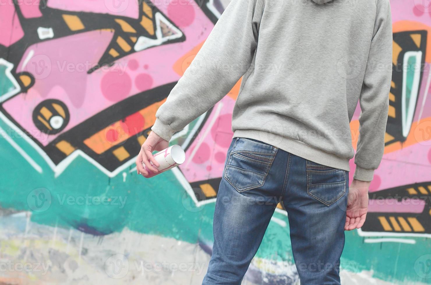 A young graffiti artist in a gray hoodie looks at the wall with photo