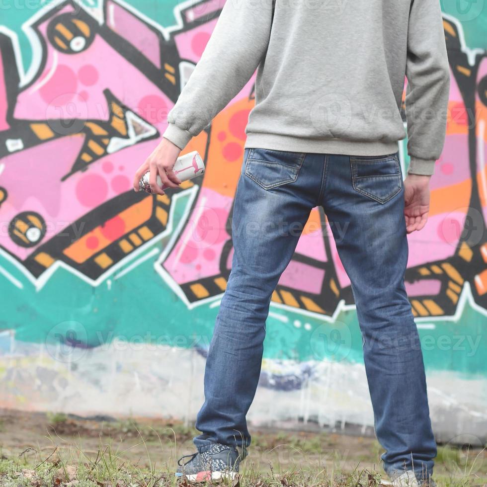 A young graffiti artist in a gray hoodie looks at the wall with photo