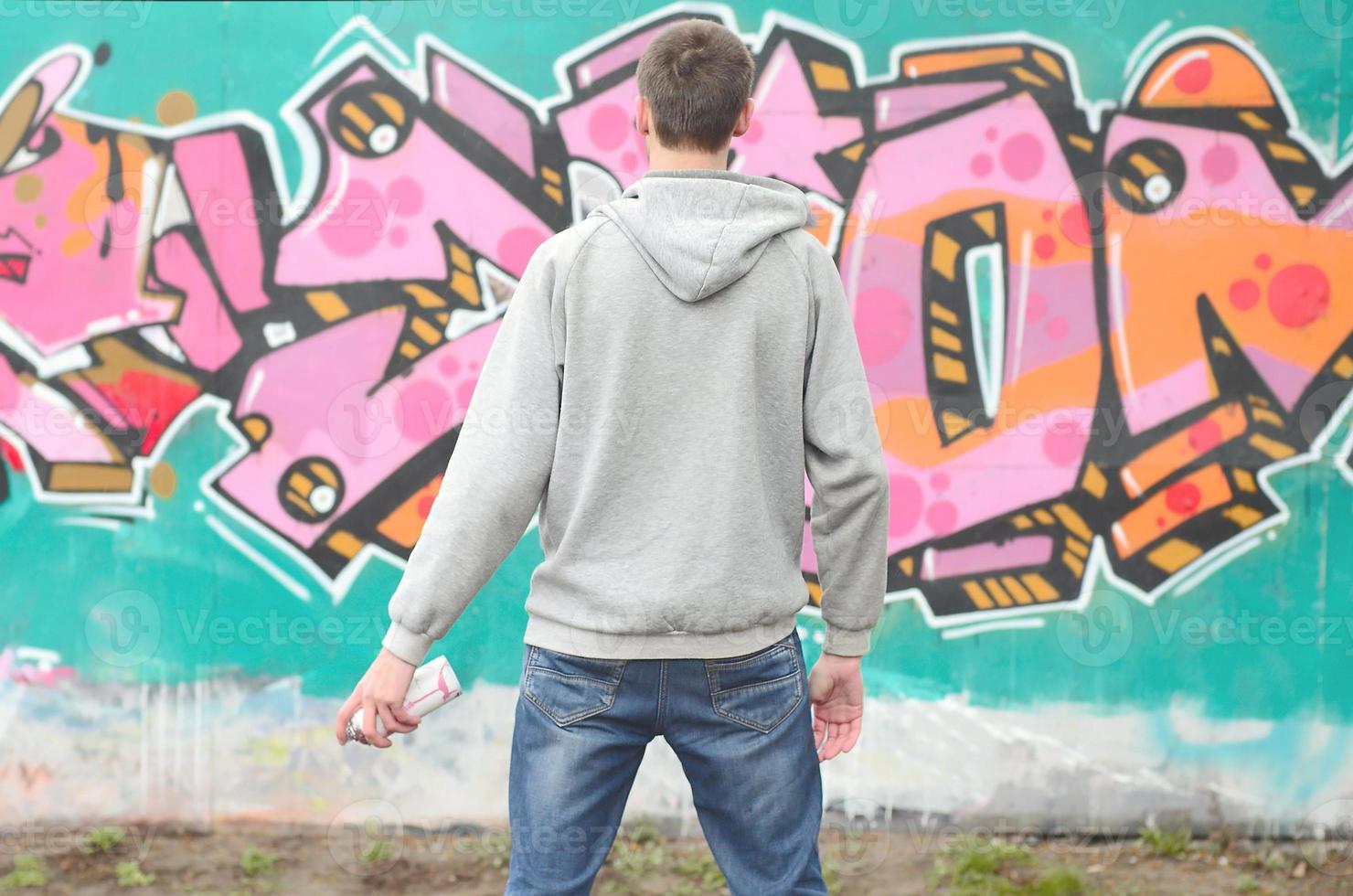 A young graffiti artist in a gray hoodie looks at the wall with photo