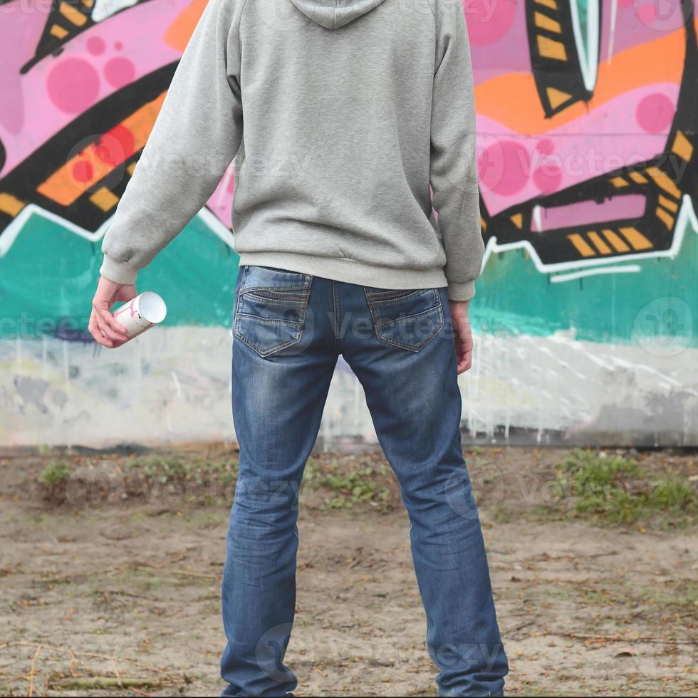 A young graffiti artist in a gray hoodie looks at the wall with photo