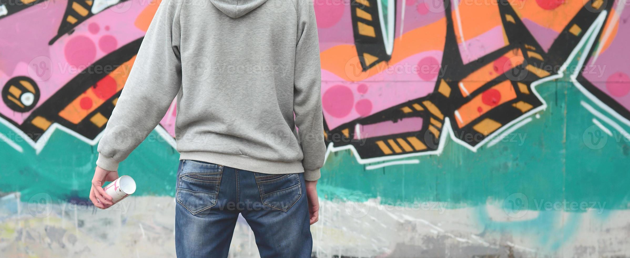 A young graffiti artist in a gray hoodie looks at the wall with photo