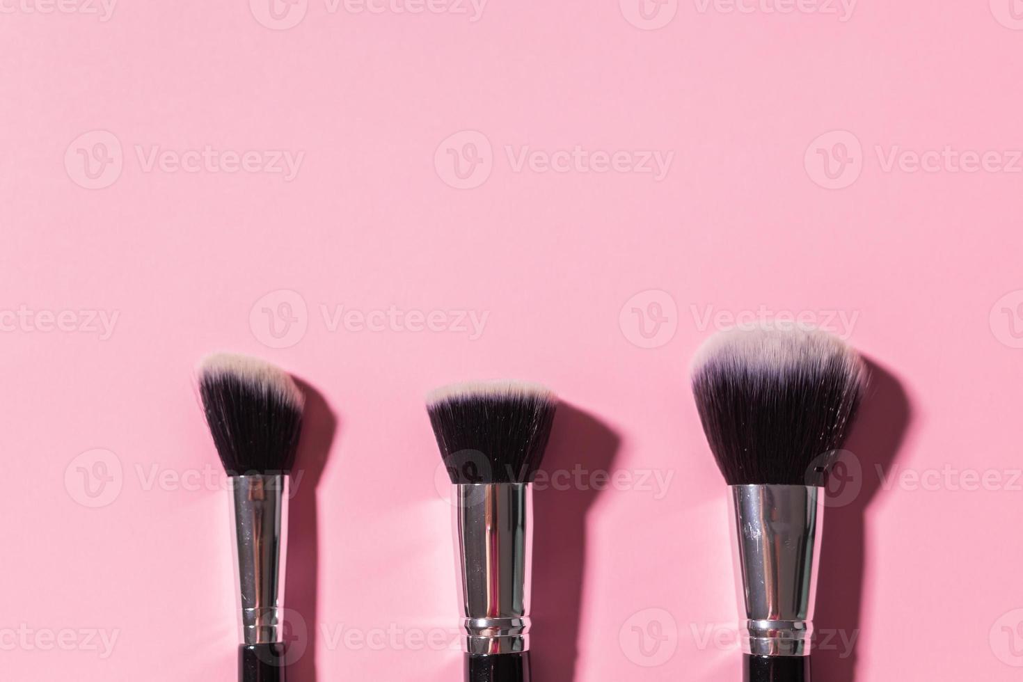 Various make-up brushes on pink background with copy space, top view. Cosmetics and beauty concept. photo