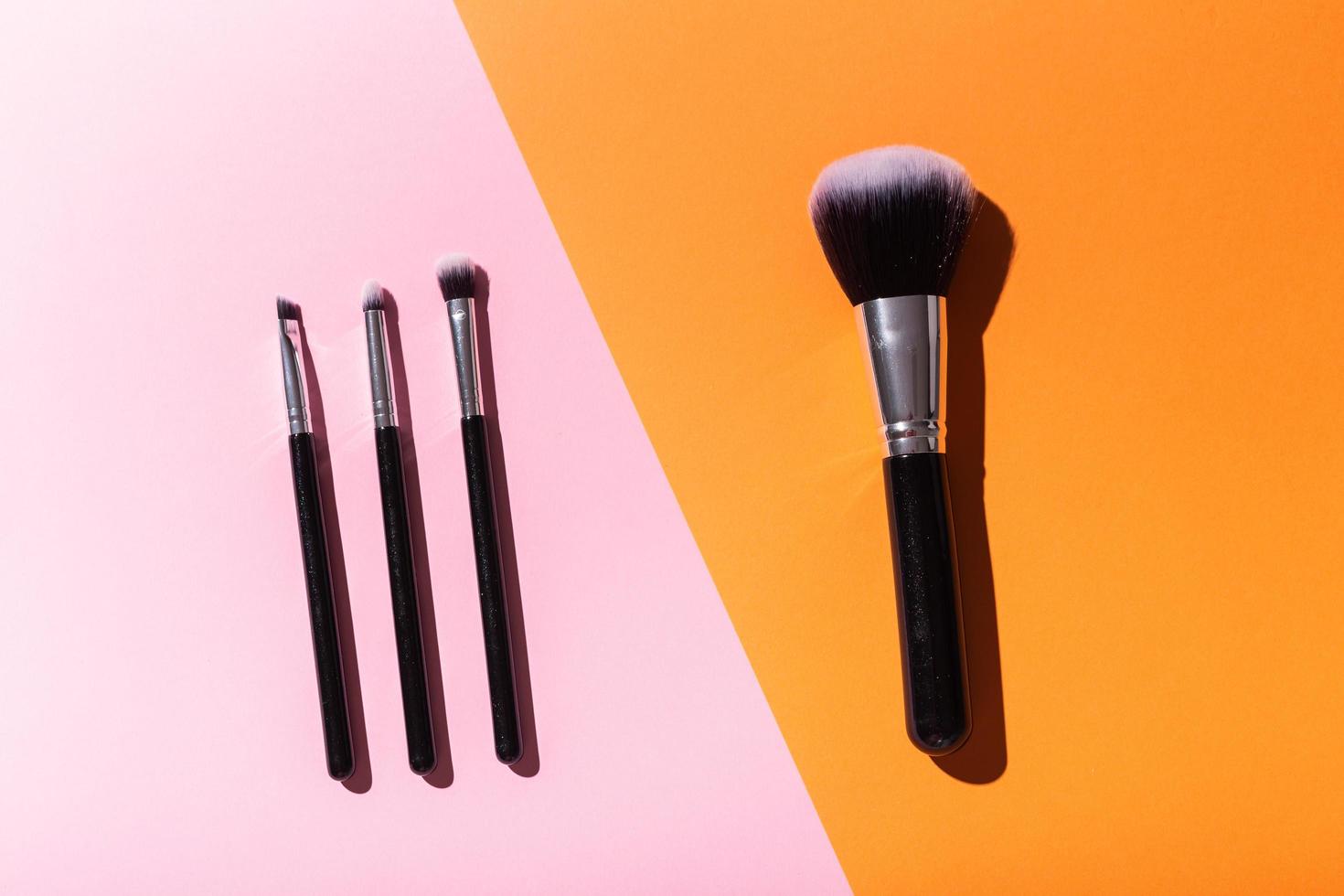 Various make-up brushes on pink and orange background, top view. Cosmetics and beauty concept. photo