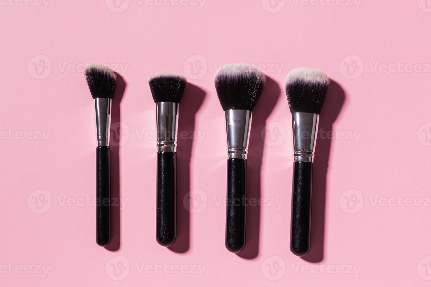 Various make-up brushes on pink background, top view. Cosmetics and beauty concept. photo