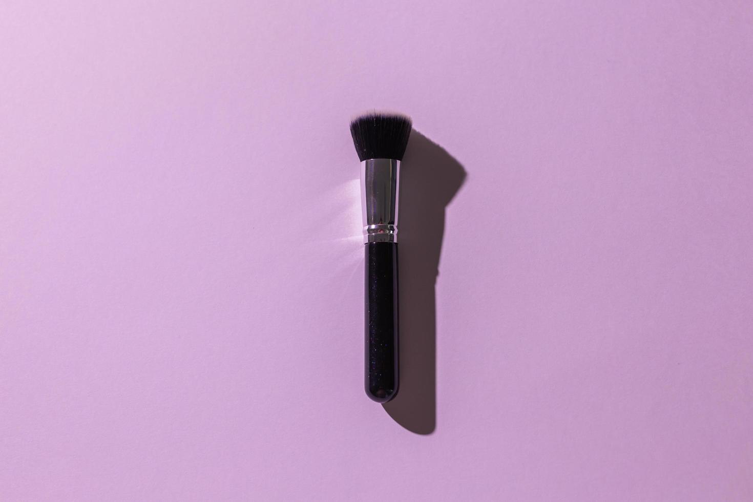 Make-up brush on lilac background, top view. Cosmetics and beauty concept. photo