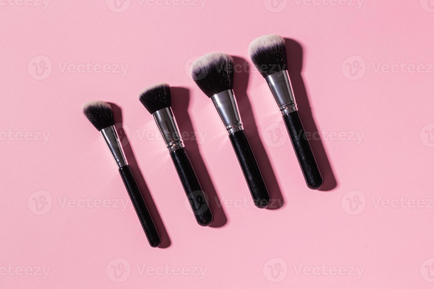 Various make-up brushes on pink background, top view. Cosmetics and beauty concept. photo