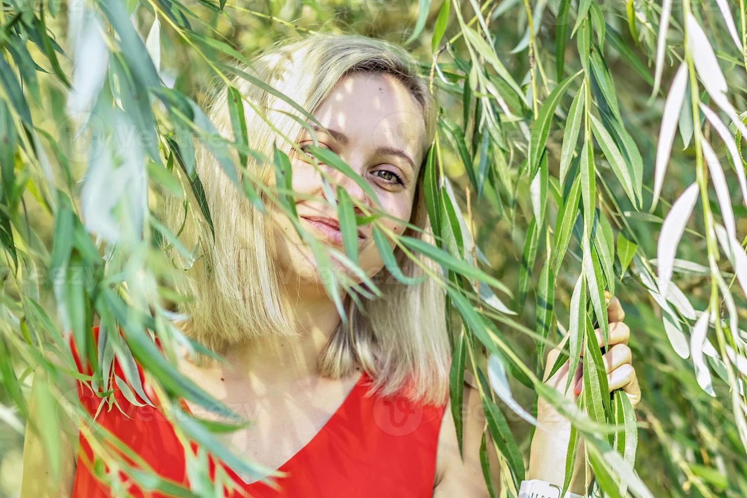 Portrait of a young blonde woman in the foliage of a weeping willow. summer time vacation photo