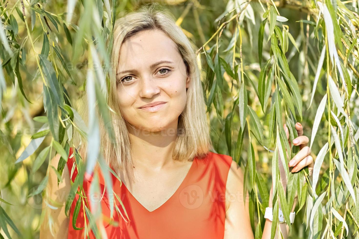 Portrait of a young blonde woman in the foliage of a weeping willow. summer time vacation photo