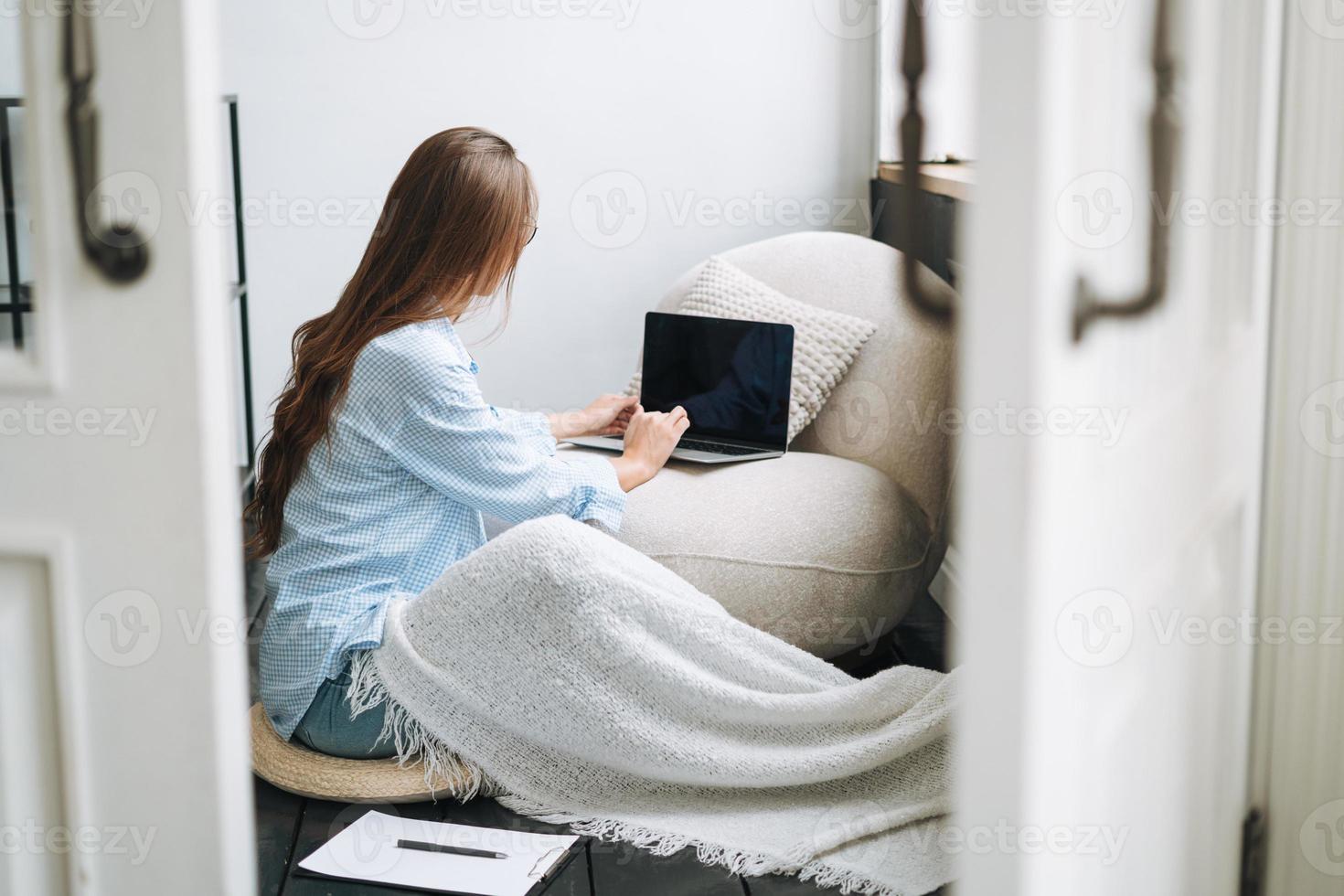 Young smiling woman in blue shirt using laptop in room, view from open doors photo
