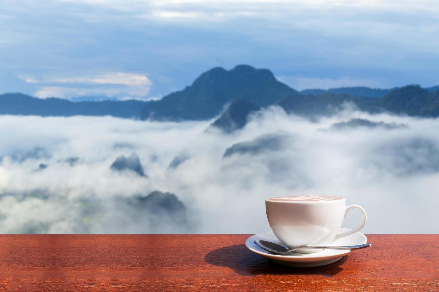 White coffee mug on wooden table, misty background and mountains  in winter at Phu Langka, Thailand photo
